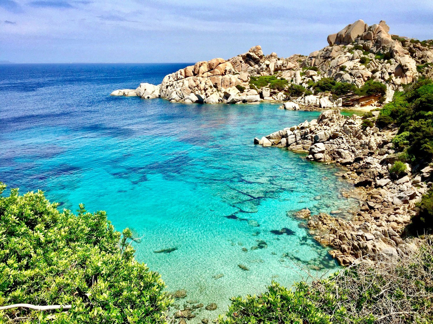 A turquoise cove between granite rocks and green macchia on the coast of Sardinia